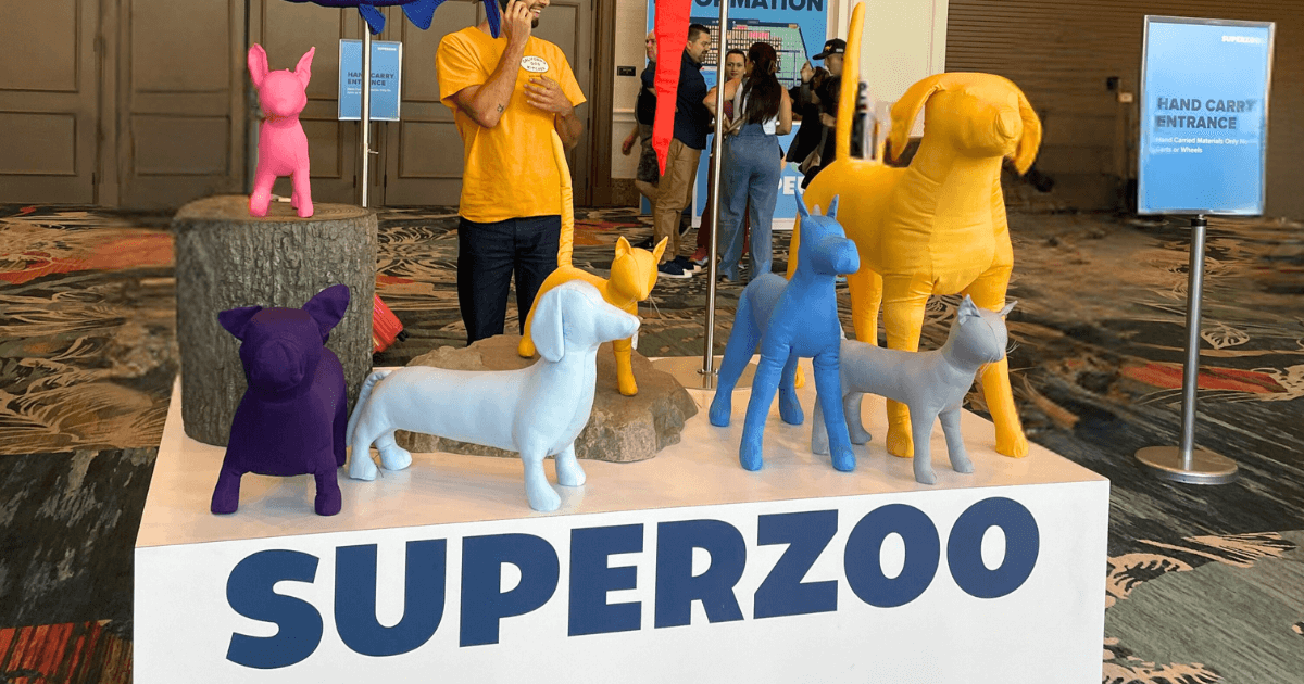 A display at SuperZoo featuring several stuffed animal dogs and cats in various colors and poses. The display is set up on a platform with the word "SUPERZOO" in large letters.