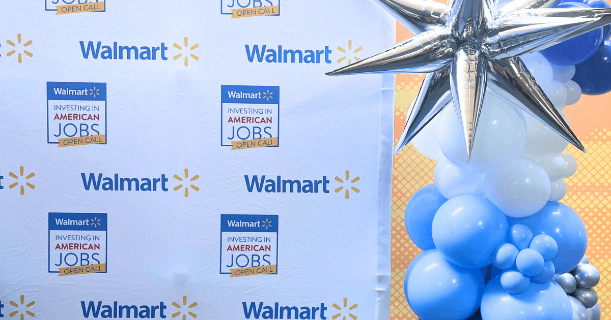 A festive display at the Walmart Open Call event with a banner repeating 'Walmart: Investing in American Jobs' and a celebratory balloon arrangement.