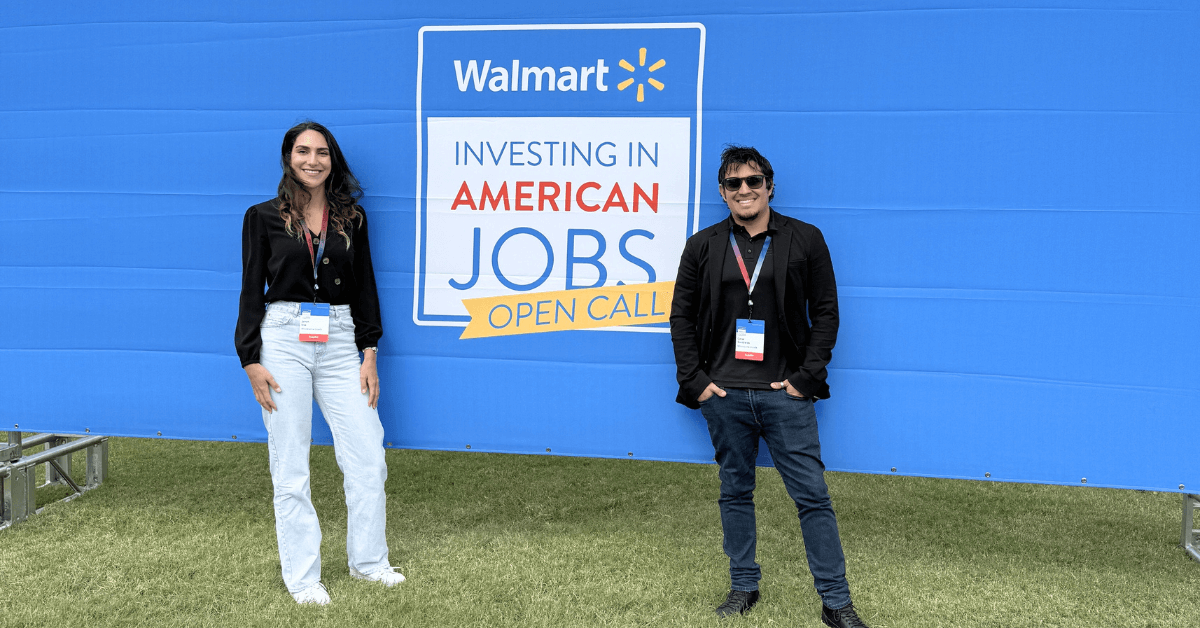 Two PupGrade team members stand smiling in front of a Walmart Open Call banner that reads 'Walmart: Investing in American Jobs.