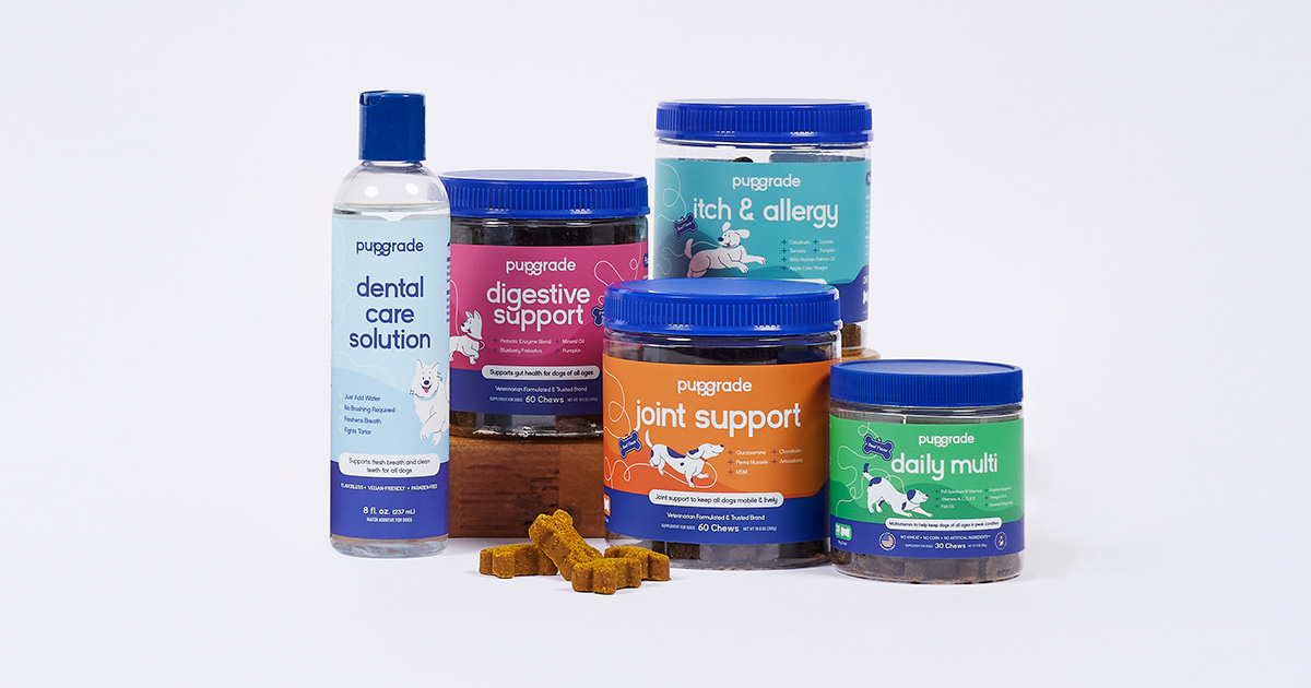 A variety of PupGrade dog supplements arranged on a light background. From left to right: a bottle of dental care solution, a container of digestive support chews, a container of itch & allergy chews, a container of joint support chews, and a container of daily multi vitamin chews.  Several bone-shaped chews are scattered in front of the containers.